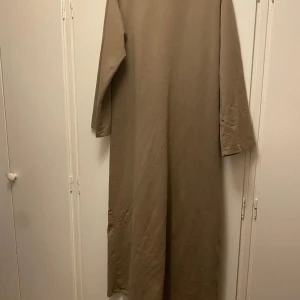 Beige långklänning abaya - Säljer en stilren beige långklänning med långa ärmar. Perfekt för en minimalistisk look. Klänningen har en enkel design utan mönster eller detaljer. Den är använd men har inga teckdn på användning. Passar storlekar XS-M och längder 155-162cm