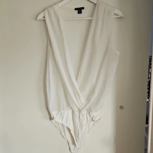 Vit bodysuit - Säljer en stilren vit bodysuit från. Den är ärmlös med djup v-ringning och har en elegant passform. Perfekt för att matcha med både kjol och byxor. Hör av dig vid intresse!