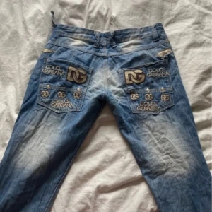 Blå lågmidjade vintage y2k flared bootcut jeans från Dolce & Gabbana - Snygga blå jeans från Dolce & Gabbana med broderad logga på bakfickorna.💓Jeansen har en klassisk femficksdesign och slitna detaljer för en trendig look. Perfekta för dig som vill ha en stilren men ändå avslappnad stil. Theres also heelbites on the back of the jeans on the 