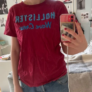 Röd t-shirt från Hollister - Säljer en röd t-shirt från Hollister med texten 'Wave Crew' i blått på framsidan. T-shirten har korta ärmar och en rund halsringning. Perfekt för en avslappnad stil. 🌊