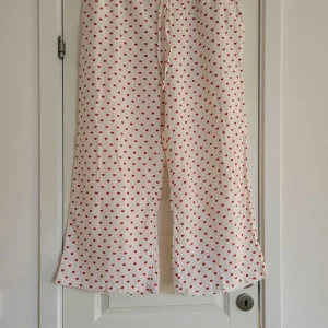 Vita pyjamasbyxor med röda hjärtan - Charmiga pyjamasbyxor med ett sött mönster av röda hjärtan. Byxorna har en loose passform och är perfekta för en avslappnad stil. De är tillverkade i ett mjukt och bekvämt material med elastisk midja för extra komfort.