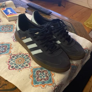 Svarta Adidas Spezial sneakers - Snygga svarta Adidas Spezial sneakers med vita detaljer och klassiska tre ränder på sidan. Skorna har en gummisula och snörning framtill. Perfekta för en stilren och sportig look.