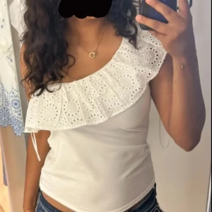 Vit oneshoulder topp  - Säljer en söt vit oneshoulder topp från hollister med en vacker spetsvolangdetalj. Säljer då den inte kommer till användning av mig. Toppen sitter som en S men är i storlek M. 