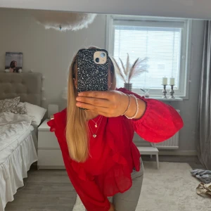 Röd blus med volanger - Säljer en snygg röd blus med volanger. Blusen har långa ärmar och en elastisk nederkant som ger en fin passform. Perfekt för att piffa upp garderoben med lite färg! Tröjan kommer från Lindex och är i storlek 158, men skulle säga snarare xs. Endast använt en gång under jul💞