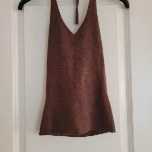 Brun stickad topp - Säljer en brun stickad topp med djup v-ringning och knytband i nacken. Perfekt för en avslappnad stil. Toppen har en mjuk och bekväm passform.