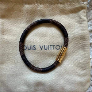 Armband från Louis Vuitton - Elegant magnetiskt armband från Louis Vuitton i brunt och svart med ett stilrent guldspänne. Perfekt accessoar för att lyfta din stil med en touch av lyx. Helt nytt, aldrig använt, låda medföljer. 