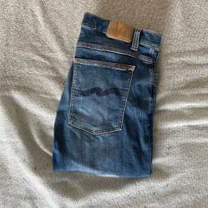 Blå jeans från Nudie Jeans - Snygga blå jeans från Nudie Jeans med klassisk femficksdesign och en diskret logga på bakfickan. Jeansen har en skinny passform och är tillverkade i högkvalitativt denim. Perfekta för en stilren look.