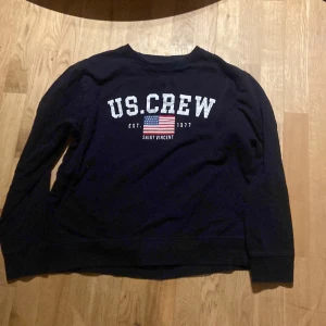 Svart tröja från Polo Club - Säljer en svart tröja från Polo Club med trycket 'US.CREW' och en amerikansk flagga på framsidan. Tröjan har långa ärmar och en rund halsringning. Perfekt för en avslappnad stil.