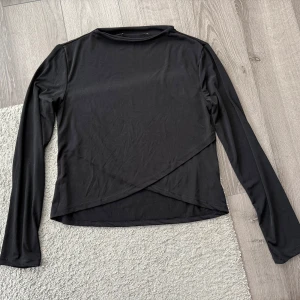 Svart omlottopp - Snygg svart omlottopp med långärmad design. Perfekt för en stilren look. Toppen har en unik omlottdetalj framtill som ger en modern touch.
