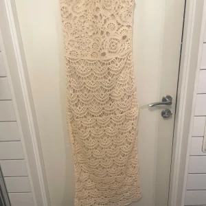 Beige spetsklänning från Zara - Säljer en elegant beige långklänning från Zara i vacker spetsdesign. Klänningen har ett intrikat mönster och är perfekt för speciella tillfällen. Den är ärmlös och har en figurnära passform som framhäver silhuetten.