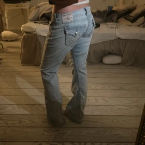 Ljusblå jeansbyxor från True Religion - Säljer ett par ljusblå jeansbyxor från True Religion, modell Joey Low Rise Flare. Byxorna har en låg midja och en utsvängd stil. De har dekorativa sömmar och en knappdetalj på bakfickan. Köpta i usa för 1200kr, modellen går inte att hitta i Sverige. Pris går att diskutera💘