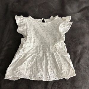 Vit blus med spetsdetaljer - Charmig vit blus med spetsdetaljer och volanger på ärmarna. Blusen har en luftig passform och en söt öppning i ryggen. Perfekt för en somrig look!