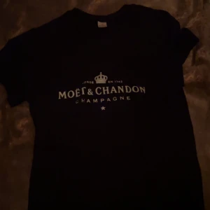 Svart t-shirt med Moët & Chandon-tryck - Snygg svart t-shirt i 100% bomull med Moët & Chandon-tryck på framsidan. Perfekt för en stilren och avslappnad look. Kortärmad och bekväm passform.