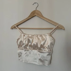 Beige satinlinne från H&M - Säljer ett stilrent beige satinlinne från H&M. Linnet har smala axelband och en glansig finish som ger en lyxig känsla. Perfekt för att klä upp en outfit eller bära som det är under varma dagar.