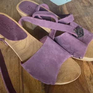 Lila sandaler med träklack från Sanita - Snygga lila sandaler från Sanita med träklack och remmar i mocka. Perfekta för sommarens alla tillfällen. De har en robust klack och en bekväm passform.