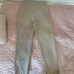 Beige kostymbyxor med raka ben - Snygga beige kostymbyxor med klassisk rak passform och bälteshällor. Byxorna har sidfickor fram och passpoalfickor bak. Perfekta för en clean och stilren look. Materialet känns mjukt och har en lätt stretch.