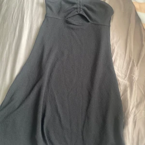 Svart omlottklänning från H&M Divided - Säljer en svart kortklänning från H&M Divided i storlek XS. Klänningen har omlottdetalj och smala axelband, med snygg rynkning och cut-out framtill. Materialet är mjukt och lätt strukturerat, perfekt för dig som gillar stilrena och trendiga plagg.
