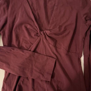 Vinröd långärmad tröja med twist - Snygg vinröd tröja med lång ärm och twistad detalj framtill som ger en cool look. Mjuk och skön bomullskvalitet, perfekt för dig som gillar stilrena plagg med en twist. Passar dig som vill ha något enkelt men ändå med lite edge.