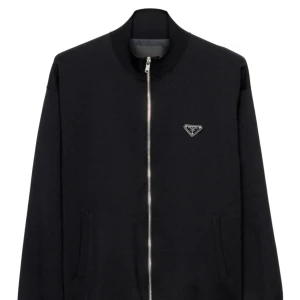 Svart zip hoodie från Prada XL - Svart hoodie från Prada i storlek XL med hel dragkedja och klassisk ståkrage. Tröjan har Pradas ikoniska metallogo på bröstet och är tillverkad i mjuk bomullsblandning. Perfekt för dig som gillar stilren och exklusiv streetwear, använd bara två gånger helt ny koster 40,000, den är i topp skick 