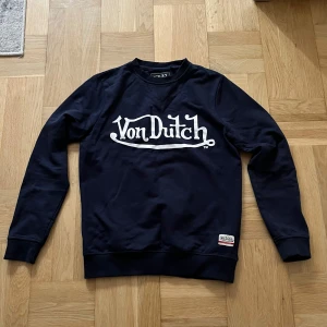 Mörkblå Von Dutch sweatshirt  - Snygg mörkblå sweatshirt från Von Dutch med stort vitt logotryck på bröstet. Tröjan har rund hals, långa ärmar och ribbade muddar. Perfekt för dig som gillar streetwear och vill sticka ut med en klassisk logga. Storlek S 