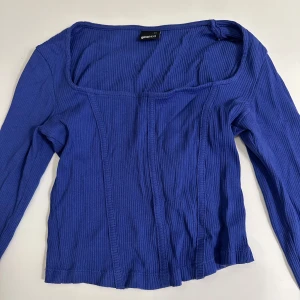 Blå ribbad topp från Gina Tricot - Blå långärmad topp från Gina Tricot i ribbat material. Toppen har en fyrkantig urringning och markerade sömmar framtill. Storlek XS passar även S. 