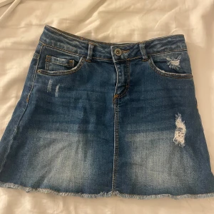 Blå jeanskjol med slitningar - Blå jeans kjol från Zara girls men passar som en xs vanlig kjol. Lågmidjad. Köpt för typ 10 år sedan men knappt använd så därför säljer jag.