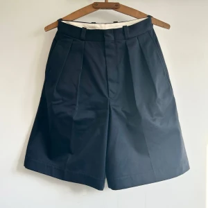 Nanamica double pleat chino shorts - Nanamica double pleat chino shorts i marinblå. Ett par knälånga vida shorts,  Storlek S, passar en 27 i midja på ett ungefär. Nypris 2500. Använda 1 gång då den var för små för mig 
