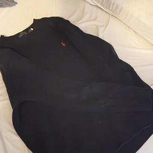 Svart stickad tröja från Polo Ralph Lauren - Svart stickad tröja från Polo Ralph Lauren med klassisk röd broderad logga på bröstet. Tröjan har rund hals, ribbade muddar och lång ärm. Perfekt för dig som gillar stilrena och tidlösa plagg med en lyxig touch. !!KÖPT I KÖPENHAMN HAN TYVÄR INGET KVITTO MEN HAR NÅRGRA BILDER!!
