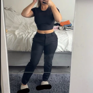 Svarta kostymbyxor med normal passform - Säljer ett par svarta kostymbyxor med klassisk look och raka ben. Byxorna har hällor för bälte, sidfickor och bakfickor med diskret knapp. Snygg midja och stilren design som passar till många outfits. Pris kan diskuteras. 