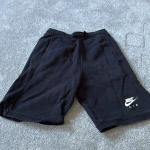 Svarta Nike Air shorts i storlek L - Nike Air shorts i svart med klassisk logga på benet. Modellen har normal passform, snörning i midjan och mjukt material som känns skönt mot huden. Perfekta för träning eller chill, med praktiska fickor på sidorna och sportig vibe.