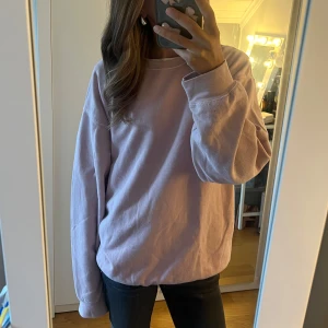 Ljusrosa sweatshirt  - Ljusrosa sweatshirt med rund hals och långa ärmar. Tröjan har en relaxed, loose passform och är tillverkad i mjuk bomull. Diskret broderad text vid halsen. Perfekt för chill dagar och enkel att matcha med jeans eller leggings.