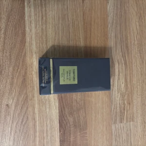 Tom Ford Tobacco Vanille EdP 100ml - Tom Ford Tobacco Vanille Eau de Parfum 100ml i elegant mörkblå kartong med gulddetaljer. Lyxig och ikonisk doft med inslag av tobak och vanilj. Förpackningen har en exklusiv känsla
