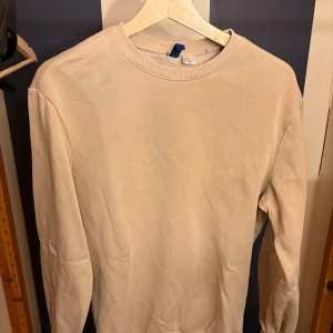 Beige sweatshirt från Divided XS - En clean beige sweatshirt från Divided i storlek XS. Tröjan har rund hals, ribbade muddar och är långärmad. Perfekt för dig som gillar enkel och stilren look. Materialet är mjuk bomull som känns skönt mot huden.