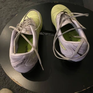 Nike Phantom GT2 fotbollsskor gul/vit - Nike Phantom GT2 fotbollsskor i en fräsch mix av ljusgul och vit med svarta detaljer. Skorna har snörning, mönstrad ovandel och dobbar för bästa grepp på planen. Perfekta för dig som vill sticka ut med stil och prestanda på matchen.
