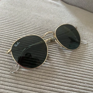 Äkta Ray-Ban RB3447 - Snygga Ray-Ban solglasögon med rund form och tunna guldfärgade metallbågar.  Glasögonen är i nyskick och säljes endast för att dom aldrig kommit till användning. Dessa inhandlades hos Synoptik, har tyvärr inget kvitto.