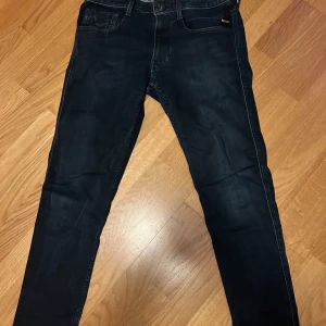 Replay Anbass jeans mörkblå, stl 32 - Säljer ett par mörkblå Replay Anbass jeans i storlek 32. Jeansen har klassisk femficksdesign, smal passform och snygga detaljer som Replay-logga och röda sömmar på bakfickan. Perfekta för dig som gillar stilrena och moderna jeans. Hör av dig om du vill veta mått osv 