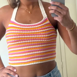 Randig virkad halternecktopp - Superfin virkad halterneck topp med färgglada ränder i vitt, rosa, oranget. Toppen är croppad och har öppen rygg med ett brett virkat band i nacken. 