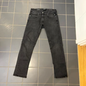 Replay Hyperflex Grover svarta jeans - Svarta Replay Hyperflex Grover jeans med klassisk femficksdesign och smal passform. Stretchigt material för extra komfort och rörelsefrihet. Snygga detaljer med metallknapp och dragkedja. Perfekta för dig som gillar stilrena och moderna jeans.