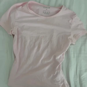 Ljusrosa t-shirt från SHEIN - Snygg ljusrosa t-shirt från SHEIN i mjuk bomull. Modellen är klassisk med rund hals och korta ärmar, perfekt för en chill och enkel stil. Passformen är normal och färgen är riktigt fräsch för sommaren.