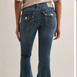 Blå bootcut jeans från True Religion - Snygga blå jeans från True Religion med bootcut passform och klassiska kontrastsömmar. Jeansen har guldiga knappar och detaljerade bakfickor med lock och dekorativa sömmar. Tillverkade i stretchig denim för en bekväm känsla. Knappast använda 