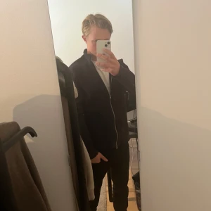 Svart stickad kofta från Only & Sons - Svart stickad kofta från Only & Sons med hel dragkedja framtill och hög krage. Tröjan har långärmad design och är gjord i ett mjukt stickat material som känns skönt mot huden. Perfekt för lager-på-lager och enkel att matcha med jeans eller chinos.