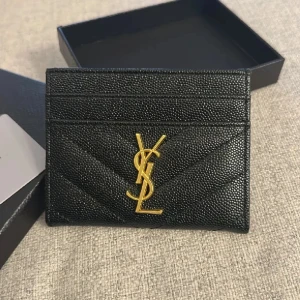 YSL korthållare  - Snygg svart plånbok från YSL i äkta skinn med quiltad struktur och guldigt YSL-logo framtill. Plånboken har flera kortfack och stilren design som passar perfekt i fickan eller väskan.