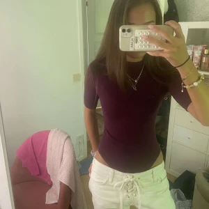 Vinröd ribbad bodysuit från H&M - Supersnygg vinröd bodysuit från H&M med ribbad struktur och korta ärmar. Modellen har en högre hals och sitter tight mot kroppen, perfekt till jeans eller kjol. Materialet är mjukt och stretchigt, vilket gör den riktigt bekväm. Skriv om du undrar något!! 🥰