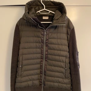 Olivgrön Moncler Cardigan - Det här är för mina större grabbar. En snygg  cardigan från Moncler med stickade ärmar och huva. Västen har quiltad framsida, dragkedja, fickor med knapp och Moncler-logga på ärmen. Perfekt lager-på-lager-plagg för kyligare dagar. Storlek XL men passar L