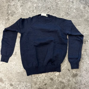 Mörkblå stickad tröja Oscar Jacobson - Mörkblå stickad tröja från Oscar Jacobson, enkel och stilren design med rund halsringning och ribbade muddar. Perfekt för lager-på-lager och passar till både jeans och chinos. Skön och mjuk känsla, passar dig som gillar klassisk stil. Stl s men passar xs