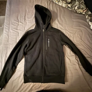 Svart hoodie från Sail racing - Säljer en svart hoodie från Sail på Racing med dragkedja framtill. Knappt använd, inge defekter, säljer på grund av ingen användning