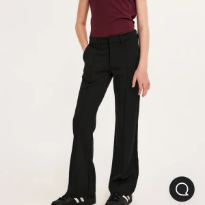 Svarta kostymbyxor från Kappahl storlek 170 - Snygga svarta kostymbyxor från Kappahl med raka ben och pressveck. Byxorna har hällor för bälte, sidfickor och en klassisk midja. Perfekta för en clean och stilren look, matcha med sneakers eller boots för en cool vibe. Storlek 170