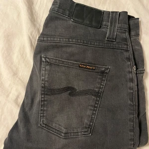 Svarta jeans från Nudie Jeans Co - Snygga svarta jeans från Nudie Jeans Co med klassisk femficksdesign och diskret logga på bakfickan. Jeansen har raka ben och normal passform, tillverkade i mjuk bomull med en lätt tvättad look. Perfekta för dig som gillar stilrena och tidlösa jeans. Tveka inte att fråga om ni undrar något eller vill ha fler bilder, Mvh Olle 