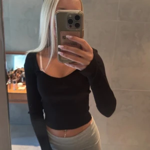 Svart ribbad croppad långärmad topp - Säljer en svart, croppad långärmad topp med ribbad struktur och snygg v-ringning. Toppen har en figurnära passform och är perfekt att styla med höga jeans eller kjol. Materialet är stretchigt och bekvämt, vilket gör den superenkel att bära till olika outfits.