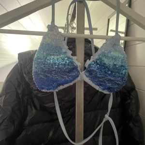 Blå paljettbikini med snörning - Säljer en ljusblå bikini från cazeldonia med glittriga paljetter i blå och silver på både överdel och underdel. Bikinin har klassisk trekantsform på toppen med snörning i nacken och ryggen. Underdelen har paljetter framtill och är enfärgad baktill. Perfekt för sommarens strandhäng!